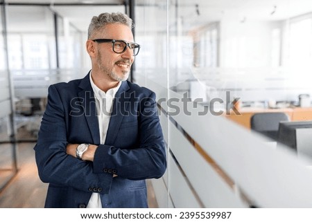 Carefree inspired 50s mature male employee standing in modern office space with arms crossed, cheerful senior gray-haired businessman in formal wear looking aside with friendly smile standing in hall