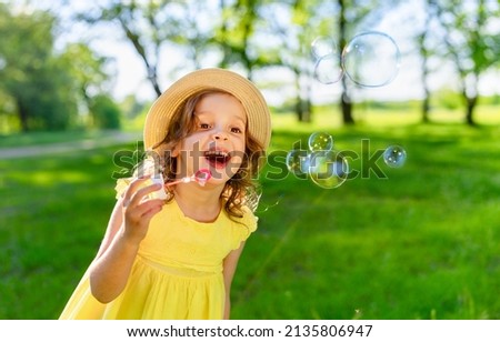 a carefree laughing girl in a bright yellow dress and a panama hat blows soap bubbles on a bright sunny day.