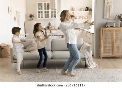 Carefree loving mom spend time with little kids at home listen music, enjoy energetic dancing to favorite song, joyful family involved in funny activity, mum teach daughter and son to dance movements - Shutterstock ID 2369161117