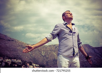 Carefree man enjoying in freedom with arms outstretched. Below view of man breathing fresh air with eyes closed. 