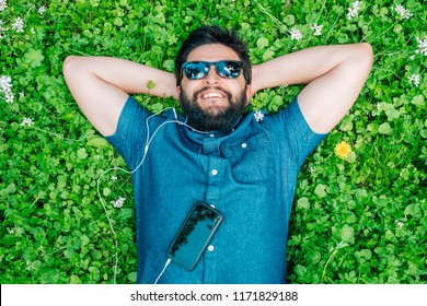 Carefree man with sunglasses lying on the grass and listening music in springtime
