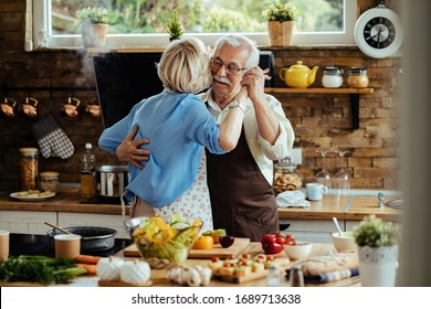 Carefree Mature Couple Dancing While Preparing Food In The Kitchen. 