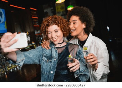 Carefree multiethnic girlfriends taking selfie and holding tequila in bar - Powered by Shutterstock