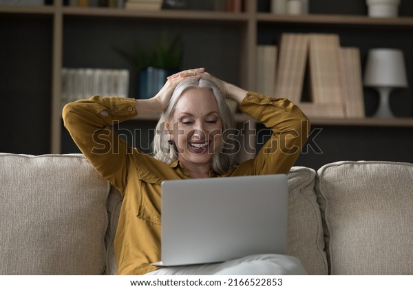 Carefree relaxed older woman put hands behind\
head looks at laptop, enjoy new series of favourite movie resting\
seated on cozy sofa. Leisure and fun at home using modern tech,\
watch on-line TV\
concept