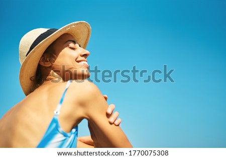 Carefree relaxed woman in hat enjoying summer beach vacation. Smiling tanned girl feeling hapiness and refreshed against bright blu sky