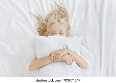 Carefree Restful Little Girl Lying On White Bedclothes, Embracing Pillow While Having Pleasant Dreams. Blonde Girl With Freckles Sleeping In Bed After Spending All Day At Picnic. Restful Child