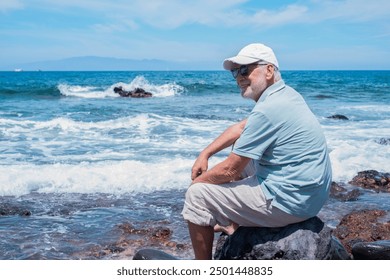 Carefree senior bearded man with cap sitting barefoot on the rocky beach enjoying summer vacation and freedom. Horizon over sea - Powered by Shutterstock