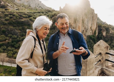 Carefree senior couple having a video call while standing on a hilltop. Happy elderly couple enjoying a recreational hike outdoors. Adventurous couple having a good time together after retirement. - Powered by Shutterstock