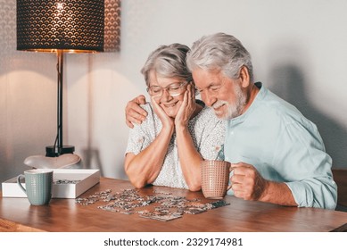 Carefree senior couple at home spend time together doing a puzzle on the wooden table. Elderly man and woman enjoying free time in retirement - Powered by Shutterstock