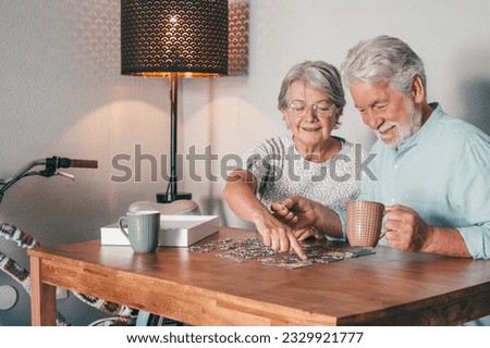 Carefree senior couple at home spend time together doing a puzzle on the wooden table. Elderly man and woman enjoying free time in retirement
