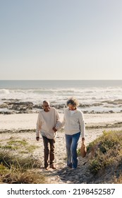 Carefree Senior Couple Smiling Happily While Walking Away From The Beach After A Picnic. Romantic Elderly Couple Enjoying A Seaside Holiday After Retirement.