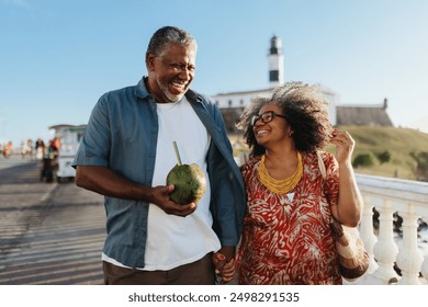 Carefree senior couple strolling and enjoying a holiday with a refreshing coconut drink under clear skies. - Powered by Shutterstock