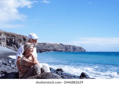 Carefree senior couple in vacation sitting on the seashore looking waves splashing on the beach enjoying retirement lifestyle and freedom, horizon over sea - Powered by Shutterstock