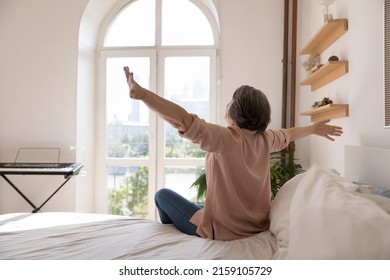Carefree senior lady feeling full of energy after sleep enough, stretching body, opening hands, looking at window. Middle aged grey haired mature woman sitting in beddings, on comfortable mattress - Powered by Shutterstock