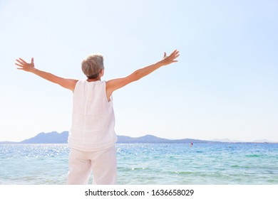 Carefree senior woman standing at beach against clear sky. Rear view of female with arms outstretched is in casuals. Tourist is enjoying summer vacation. - Powered by Shutterstock