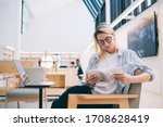 Carefree student reading literature best seller while e learning in coworking space with high speed internet connection for web browsing via laptop netbook,youthful woman in glasses checking book plot