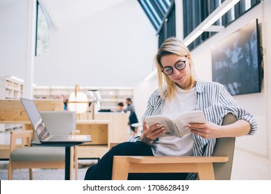 Carefree Student Reading Literature Best Seller While E Learning In Coworking Space With High Speed Internet Connection For Web Browsing Via Laptop Netbook,youthful Woman In Glasses Checking Book Plot