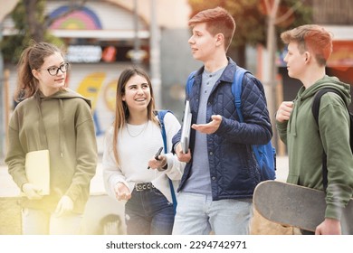 Carefree teen students walking outside school building and friendly talking in sunny spring day