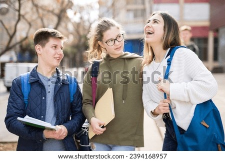Carefree teenage friends friendly talking near college building after lessons in sunny day