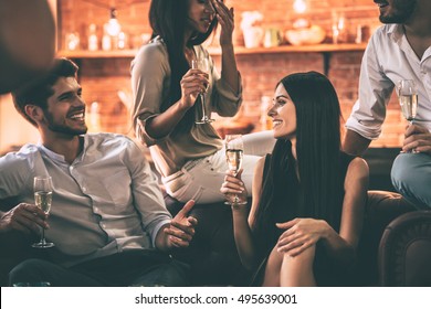 Carefree time with best friends. Group of cheerful young people enjoying food and drinks while spending nice time in cofortable chairs at home together - Powered by Shutterstock