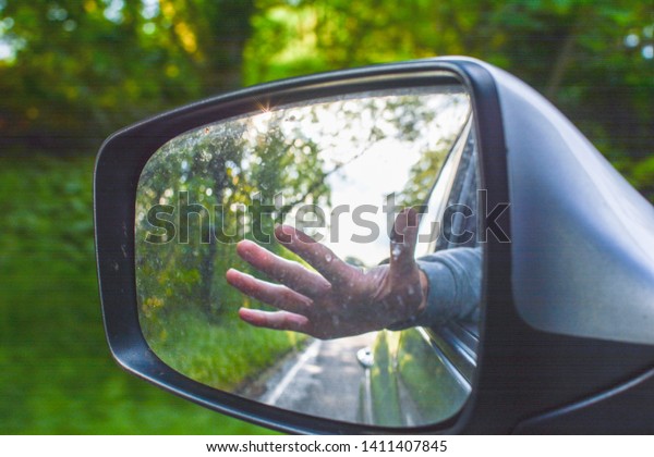 Carefree traveller with hand out passenger side\
window of car on a road\
trip