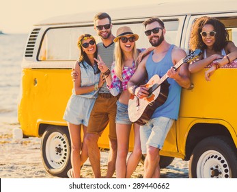 Carefree weekend with friends. Group of young cheerful people bonding to each other and smiling while leaning at their retro styled minivan with sea in the background - Powered by Shutterstock