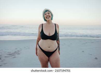 Carefree winter bather smiling with her eyes closed while standing by the sea. Happy middle aged woman standing at the beach in swimwear. Female winter bather enjoying the cold weather.
