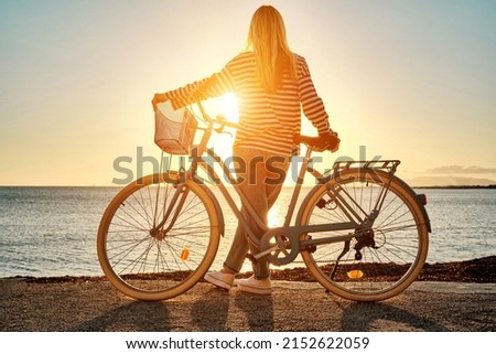 Carefree woman with bike riding on sand beach having fun, on the seaside promenade on a summer day.