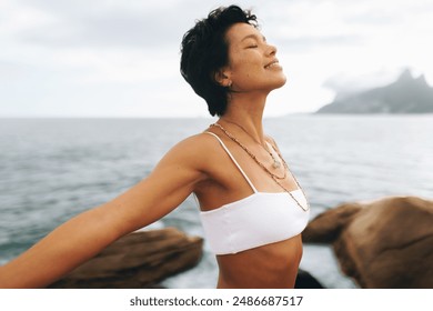 Carefree woman in bohemian jewelry with wavy hair poses at the seaside beach, enjoying a peaceful and joyful moment by the ocean. - Powered by Shutterstock