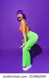 Carefree Woman Dancer Wearing Colorful Sportswear Twerking Against Purple Background