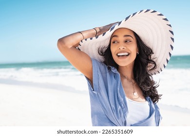 Carefree woman with white and blue straw hat walking at beach. Young smiling latin woman on vacation enjoying sea breeze. Attractive hispanic girl relaxing at beach with the sea behind. - Powered by Shutterstock
