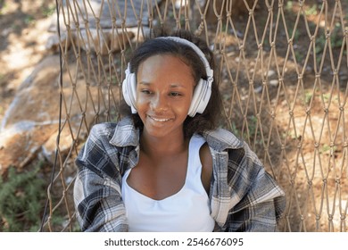 Carefree young African American woman relaxing on a hammock, enjoying listening to music through wireless headphones, and the beautiful nature around her. - Powered by Shutterstock