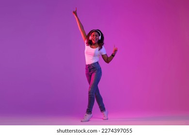 Carefree Young Black Woman Wearing Wireless Headphones Listening Music And Dancing In Bright Neon Light Over Purple Studio Background, Happy Positive African American Lady Enjoying Favorite Playlist - Powered by Shutterstock