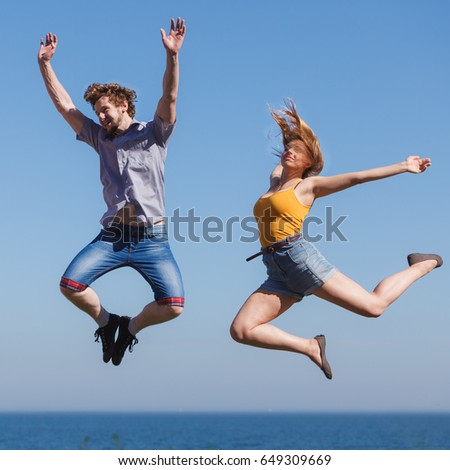 Carefree young couple friends jumping by sea ocean water. Happy woman and man having fun. Summer happiness and freedom.