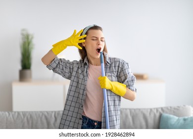 Carefree young housewife in rubber gloves using mop as mic and singing, cleaning modern apartment. Millennial maid having fun during domestic chores, enjoying her favorite song - Powered by Shutterstock