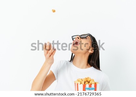 Carefree young woman in 3D glasses eating popcorn tossing it in her mouth, having fun while watching movie, white studio background