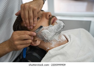 Careful Barber Using Straight Razor To Shave Man Face