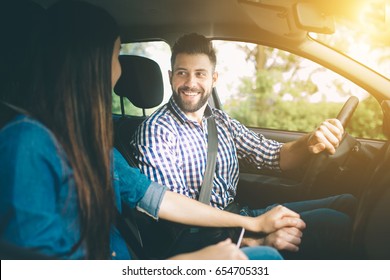 Careful driving. Beautiful young couple sitting on the front passenger seats and smiling while handsome man driving a car - Powered by Shutterstock