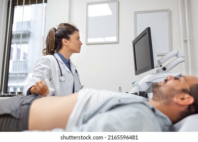 Careful female doctor in white coat sitting in front of an ultrasound apparatus and conducting abdominal diagnostics with transducer - Powered by Shutterstock