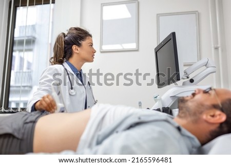 Careful female doctor in white coat sitting in front of an ultrasound apparatus and conducting abdominal diagnostics with transducer