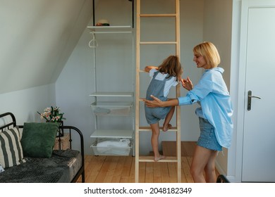 Careful mother helping her daughter to climb up the ladder in the living room - Powered by Shutterstock