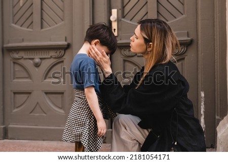 Careful mother pities the son. Woman hugs boy standing near door outside.  Mother sat down to her son and hugs him tightly. Childhood, parenthood concept.