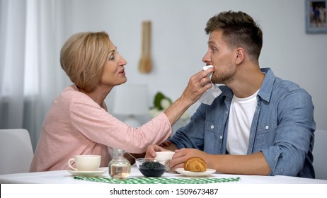 Careful mother wiping adult sons mouth during having tea at home, overprotection - Powered by Shutterstock