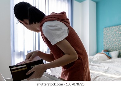 Careful Teenager girl opens a wallet and pulls cash with her hand from the purse,asian woman is quietly trying to steal her parents money in a bedroom at home,bad behavior,concept of theft,burglary
