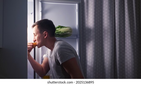 Careful Young Man Opens Door Of Modern Fridge And Eats Delicious Creamy Eclair In Secret Turning Back In Dark Empty Kitchen At Night