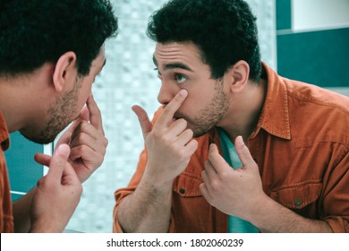 Careful Young Man Standing In Front Of A Mirror And Pulling One Lower Eyelid Further Down With His Finger