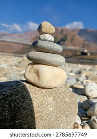 A carefully balanced stack of river stones or cairn on the banks of the Yargyap Chu river in Mechuka Valley, Arunachal Pradesh, Northeast India. The Mechuka hanging bridge and snow-capped Himalayan mountains are visible in the background. Mechuka is a remote valley near the Indo-Tibet border.2023,03,22