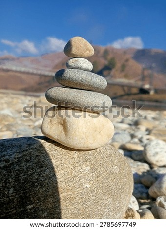 A carefully balanced stack of river stones or cairn on the banks of the Yargyap Chu river in Mechuka Valley, Arunachal Pradesh, Northeast India. The Mechuka hanging bridge and snow-capped Himalayan mountains are visible in the background. Mechuka is a remote valley near the Indo-Tibet border.2023,03,22