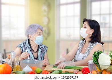 Caregiver or companion and senior adult woman speak in a friendly manner as they cook a vegetable salad together. Both are wearing protective face masks due to the coronavirus pandemic now. 