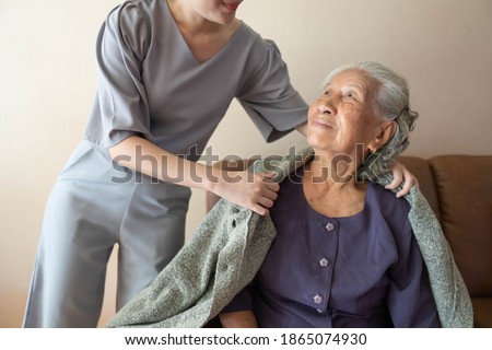 Caregiver covering senior woman with sweater at home. Happy elderly patient with friendly female nurse spending time together. Stockfoto © 